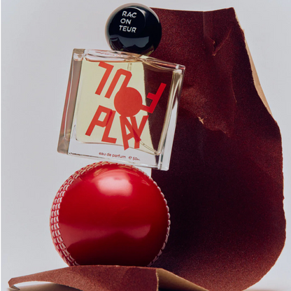 Perfume bottle labeled 'Foul Play' with a red ball and sandpaper on a light gray background